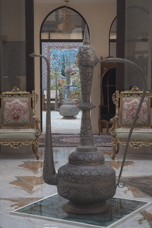 : Ornate metal vessel with long spout and engraved details displayed indoors.