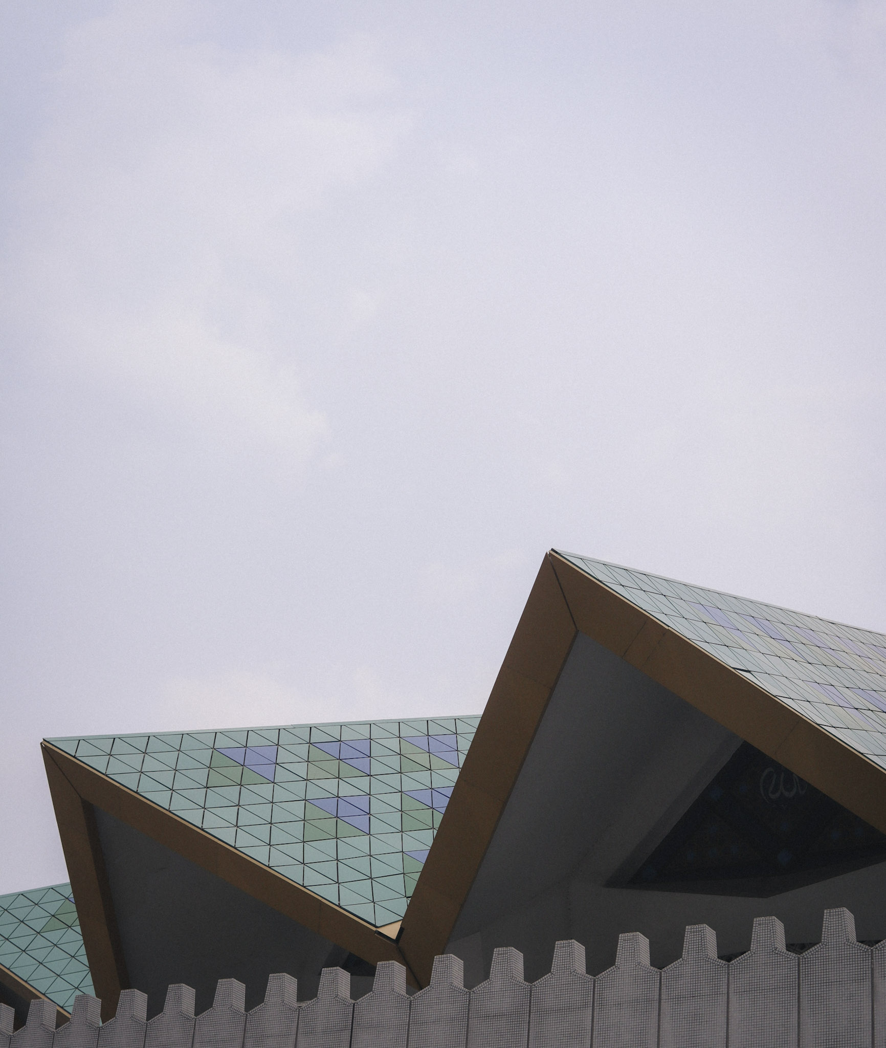 Low-angle view of the geometric roof of Masjid Negara in Kuala Lumpur, with patterned tiles, sharp architectural lines, and a pale sky above.
